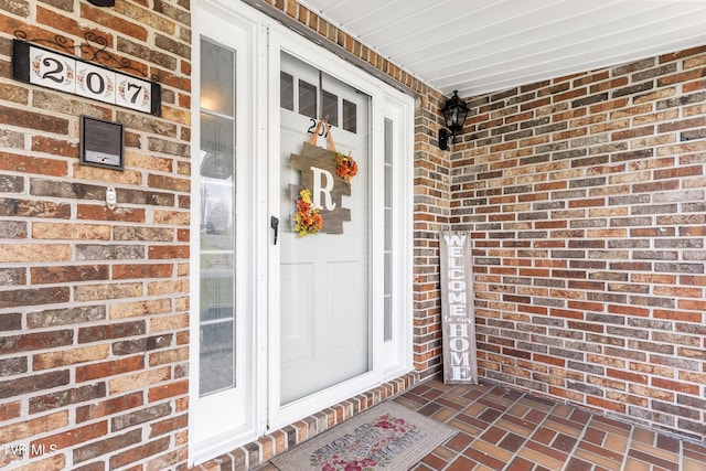 view of exterior entry featuring a porch and brick siding