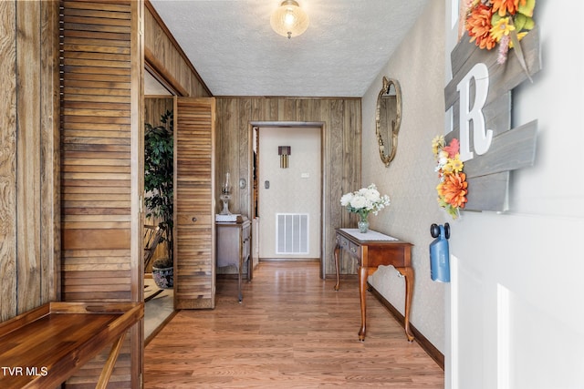 interior space featuring light wood-type flooring, wood walls, visible vents, and a textured ceiling