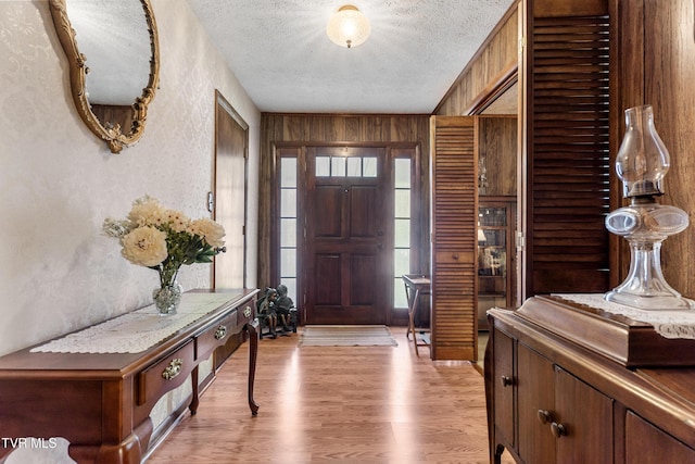 entryway with wooden walls, light wood-type flooring, a textured wall, and a textured ceiling