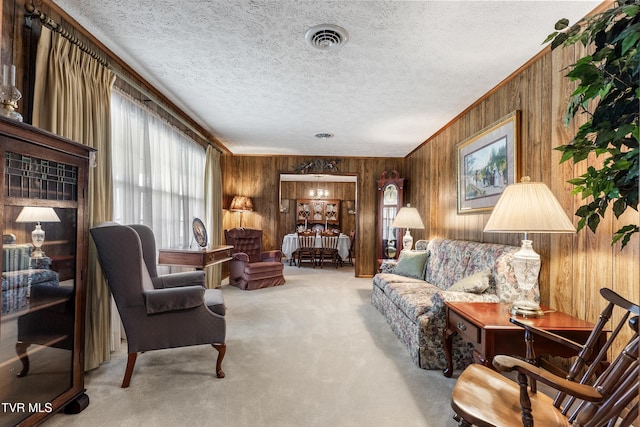 carpeted living area with wood walls, crown molding, visible vents, and a textured ceiling