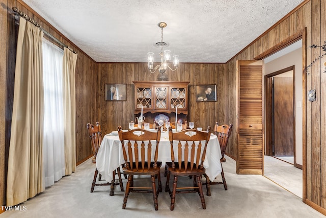 dining space with a textured ceiling, light carpet, wood walls, ornamental molding, and an inviting chandelier