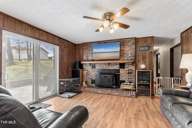 living area featuring a textured ceiling, wooden walls, a ceiling fan, and wood finished floors