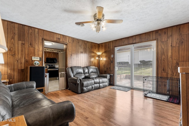 living room with a textured ceiling, a ceiling fan, light wood-style flooring, and wooden walls