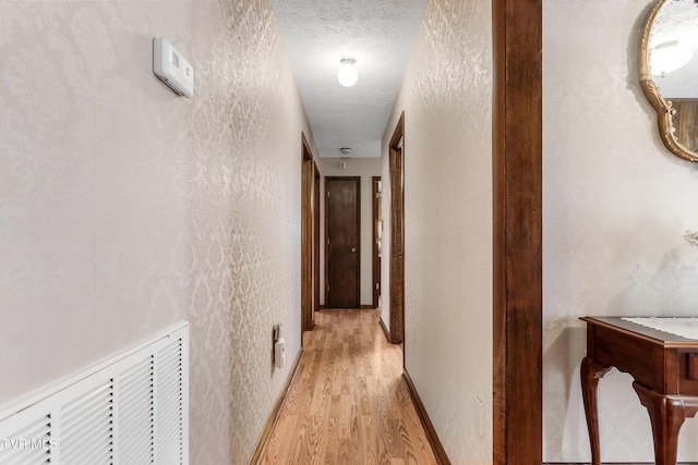 hallway featuring a textured ceiling, light wood-style flooring, and baseboards