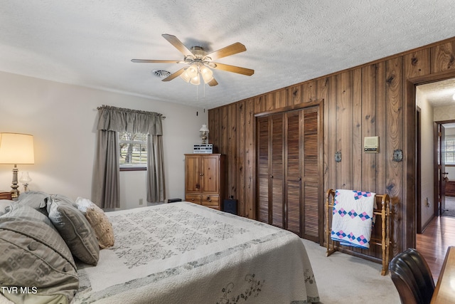 carpeted bedroom featuring a textured ceiling, ceiling fan, wood walls, and a closet