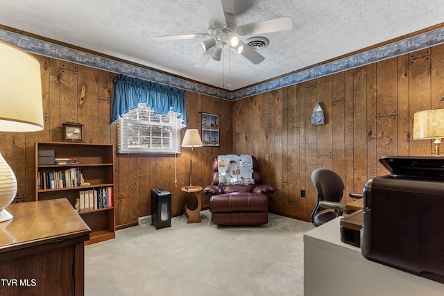 carpeted home office with a textured ceiling, visible vents, a ceiling fan, and wooden walls