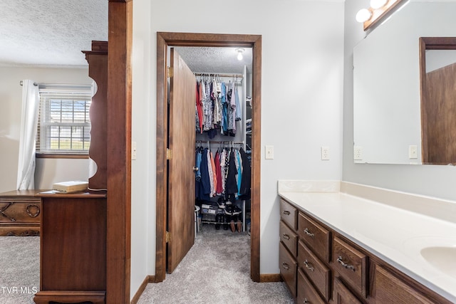 bathroom with baseboards, a textured ceiling, vanity, and a spacious closet