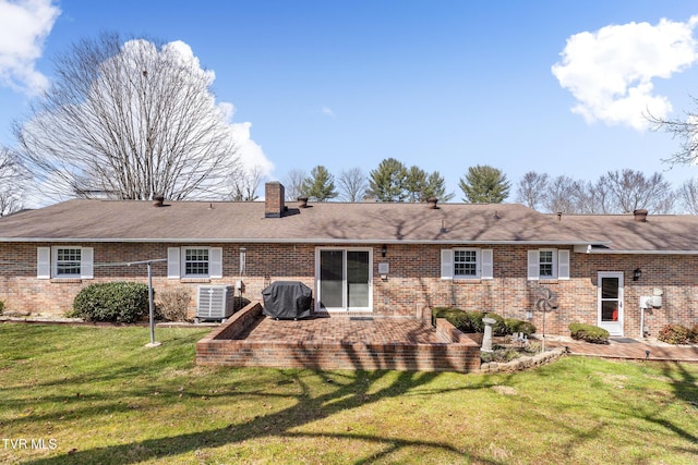 back of house featuring a chimney, a lawn, central AC, and brick siding