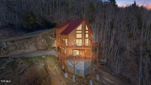 back of property at dusk featuring aphalt driveway and a wooded view