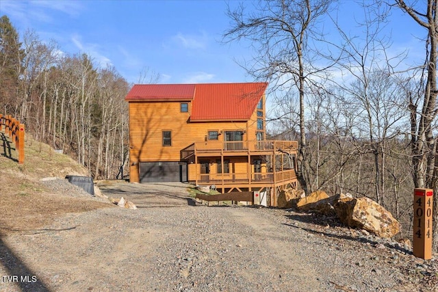 view of front of house featuring driveway, a garage, a deck, and metal roof