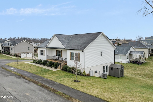 view of front of property featuring an outbuilding, roof with shingles, a residential view, a shed, and a front lawn