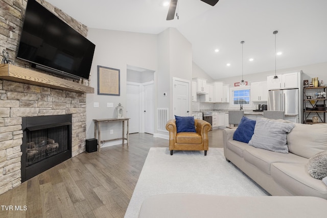 living room featuring visible vents, ceiling fan, light wood-style floors, a fireplace, and high vaulted ceiling