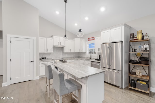 kitchen with a kitchen island, light stone counters, stainless steel appliances, light wood-type flooring, and a sink