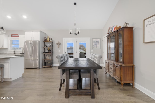 dining space featuring lofted ceiling, light wood-style flooring, a chandelier, and baseboards