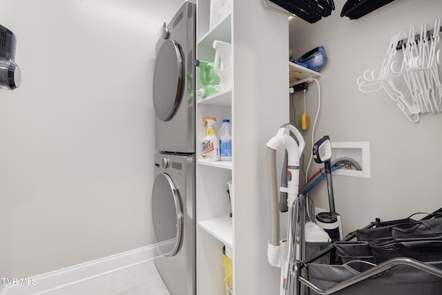 clothes washing area featuring stacked washer / dryer, laundry area, tile patterned flooring, and baseboards