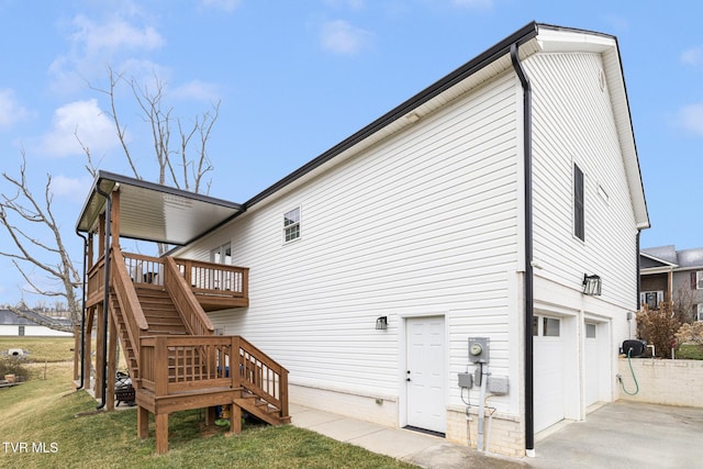 rear view of property with a wooden deck, concrete driveway, stairway, an attached garage, and a yard