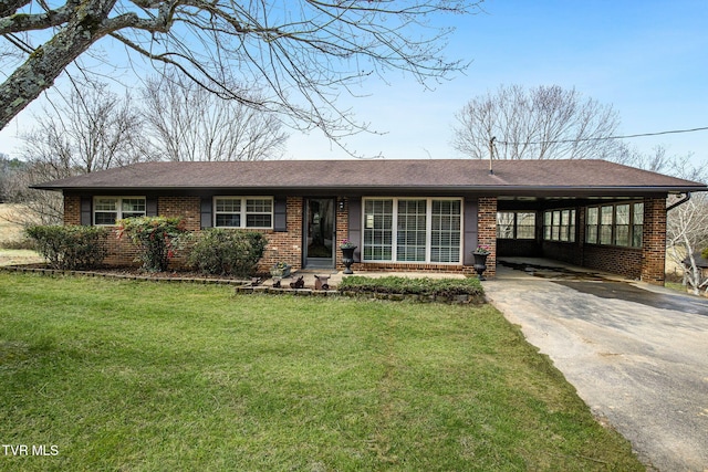 ranch-style house featuring brick siding, roof with shingles, a carport, driveway, and a front lawn