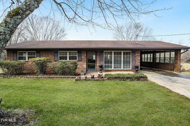 ranch-style home with brick siding, a shingled roof, a front yard, a carport, and driveway