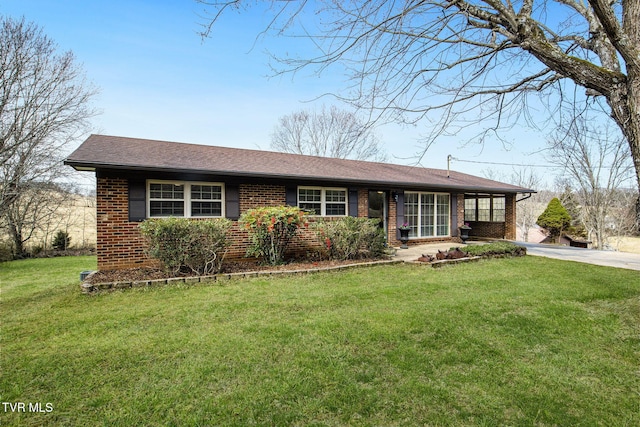 ranch-style home featuring driveway, brick siding, roof with shingles, and a front yard