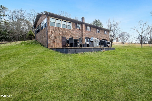 rear view of property featuring a yard, a chimney, and brick siding