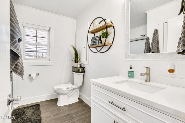 bathroom featuring baseboards, toilet, wood finished floors, crown molding, and vanity