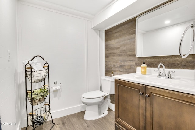 bathroom featuring toilet, wooden walls, wood finished floors, and vanity