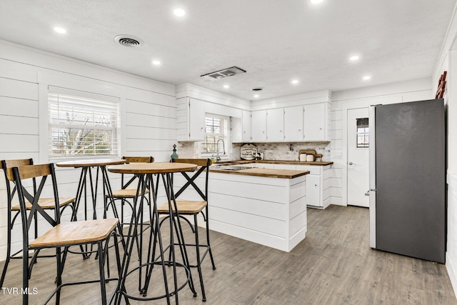 kitchen with butcher block countertops, freestanding refrigerator, visible vents, and wood finished floors