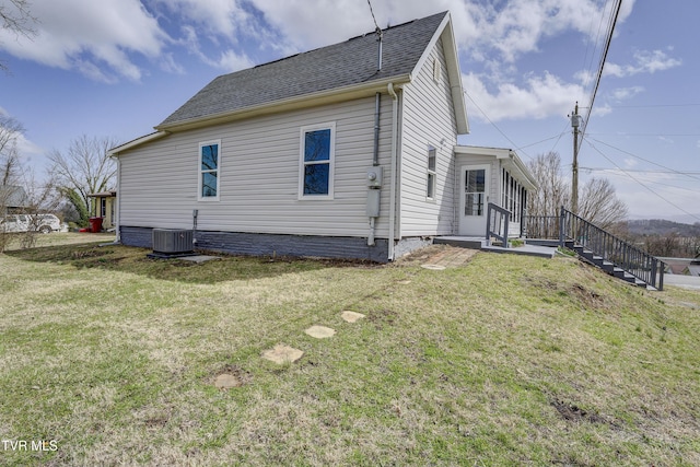 view of side of home featuring a yard, central AC, and roof with shingles