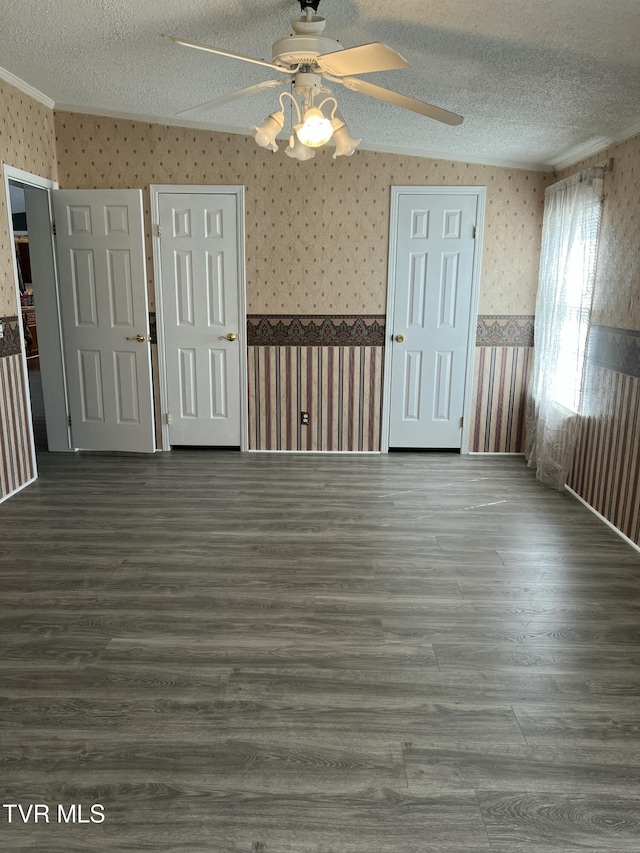 unfurnished room featuring wallpapered walls, wood finished floors, a textured ceiling, and wainscoting