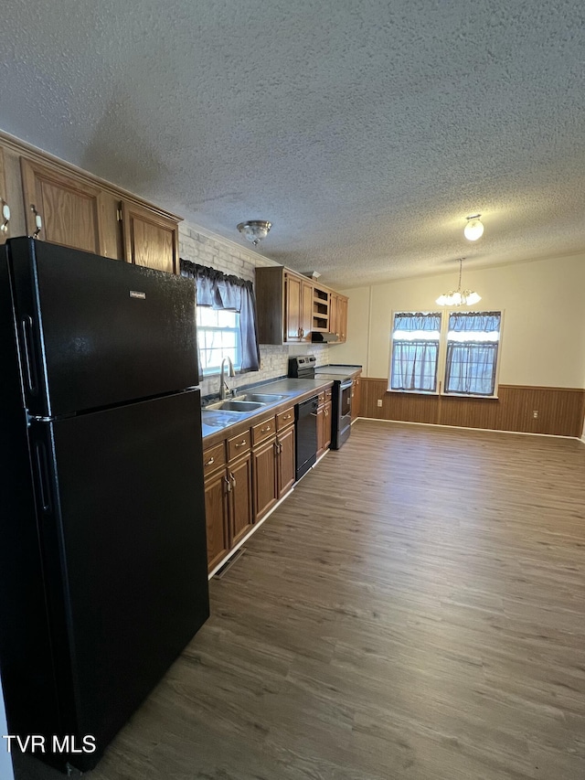 kitchen with a wainscoted wall, black appliances, a sink, and dark wood-style floors