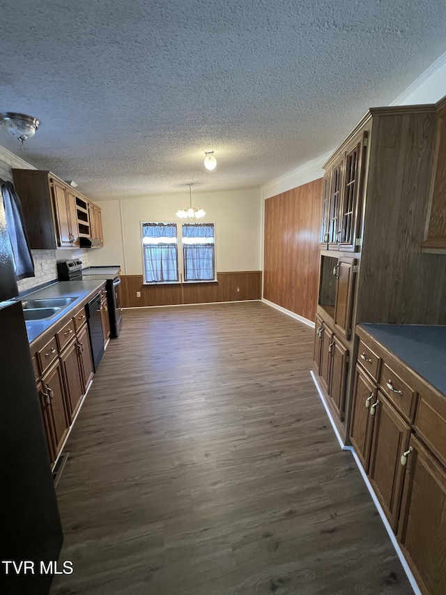 kitchen featuring a wainscoted wall, dark wood-type flooring, dark countertops, glass insert cabinets, and an inviting chandelier