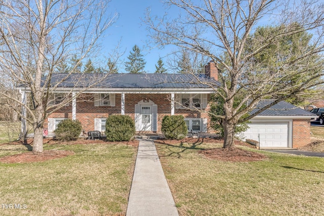 raised ranch featuring metal roof, brick siding, a front lawn, and a chimney