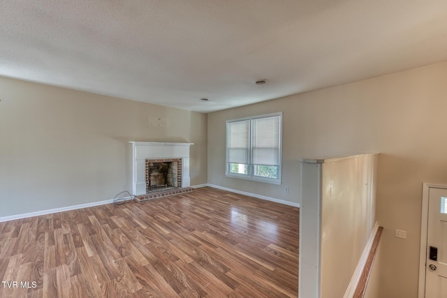 unfurnished living room featuring a textured ceiling, wood finished floors, visible vents, baseboards, and a brick fireplace