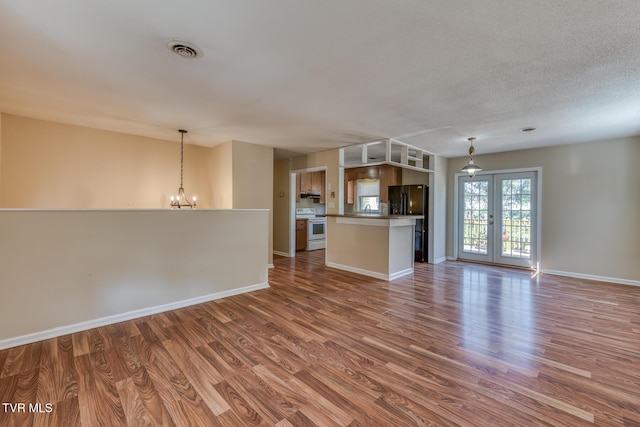 unfurnished living room featuring a chandelier, wood finished floors, visible vents, baseboards, and french doors