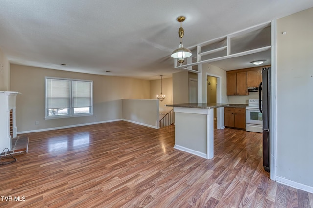 kitchen with under cabinet range hood, wood finished floors, open floor plan, electric stove, and brown cabinets