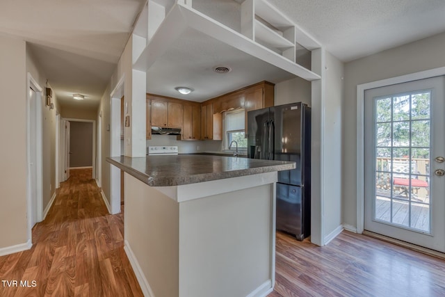 kitchen with under cabinet range hood, wood finished floors, baseboards, black refrigerator with ice dispenser, and dark countertops