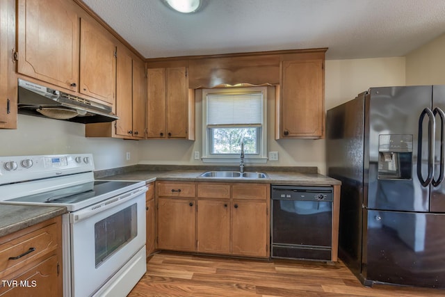 kitchen featuring light wood finished floors, dark countertops, a sink, under cabinet range hood, and black appliances