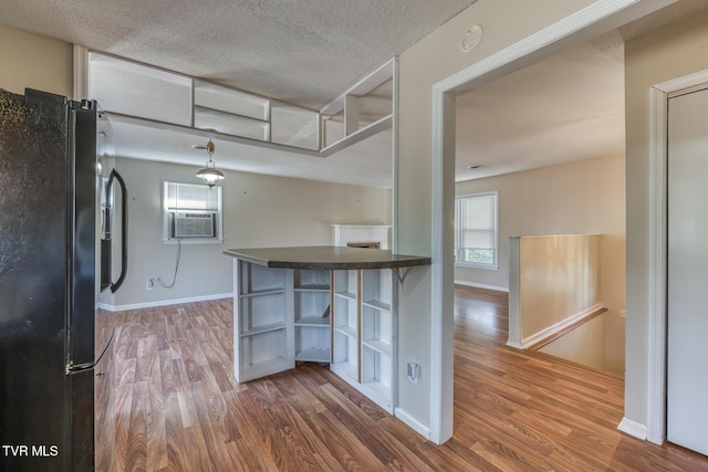 kitchen with a textured ceiling, wood finished floors, black fridge with ice dispenser, open shelves, and dark countertops