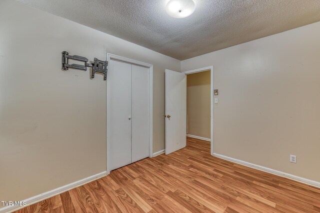 unfurnished room with a textured ceiling, light wood-type flooring, and baseboards