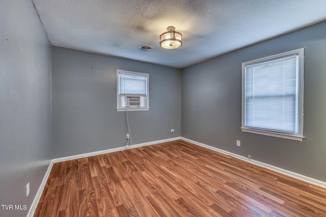 unfurnished room with visible vents, a textured ceiling, baseboards, and wood finished floors