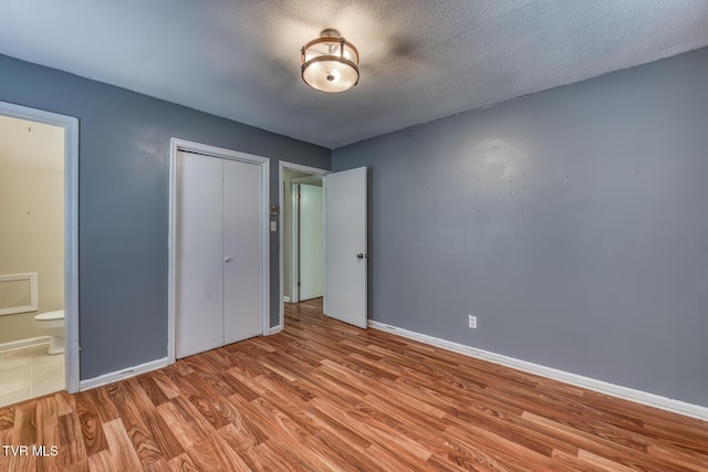 unfurnished bedroom featuring a textured ceiling, a closet, wood finished floors, and baseboards