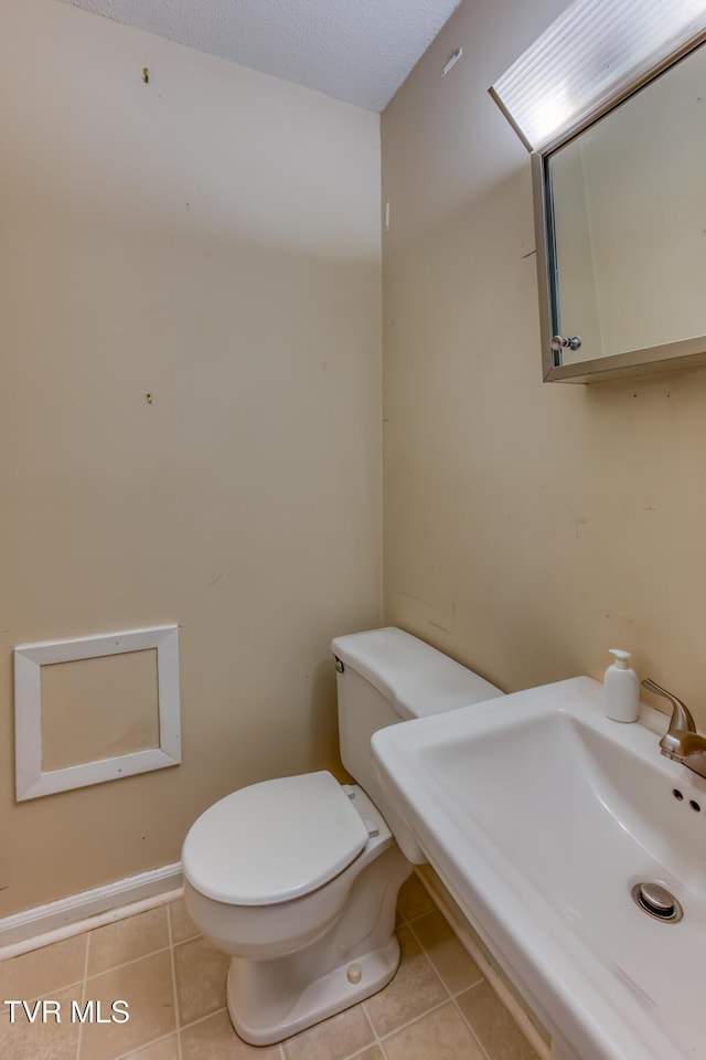 half bathroom with tile patterned flooring, baseboards, a sink, and toilet