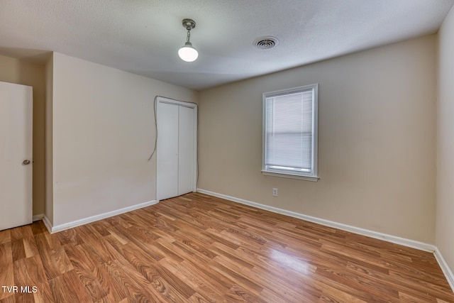 spare room featuring light wood finished floors, baseboards, visible vents, and a textured ceiling