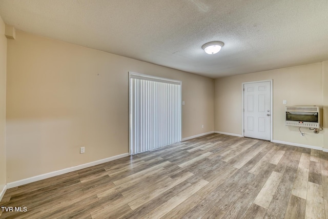 unfurnished room featuring baseboards, a textured ceiling, heating unit, and wood finished floors