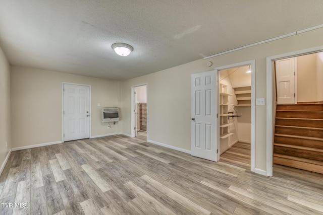 unfurnished room featuring heating unit, light wood-style floors, a textured ceiling, baseboards, and stairs