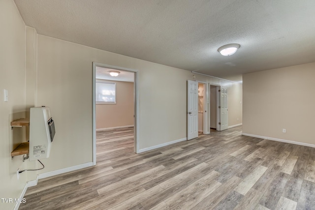 empty room featuring a textured ceiling, baseboards, heating unit, and light wood-style floors