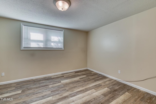 spare room with a textured ceiling, wood finished floors, and baseboards