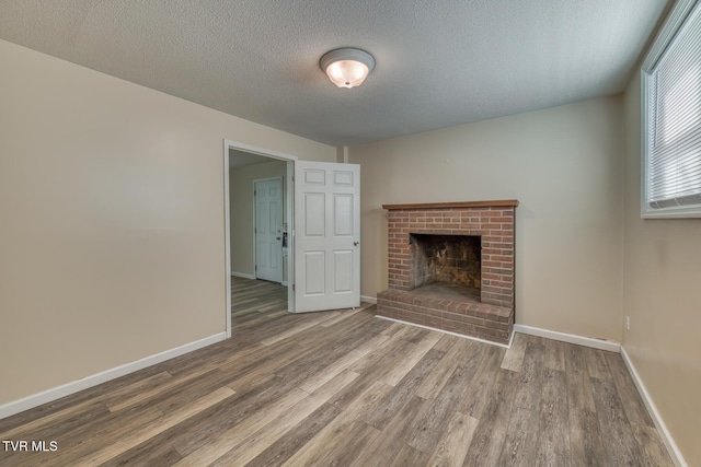 unfurnished living room featuring a textured ceiling, a fireplace, baseboards, and wood finished floors