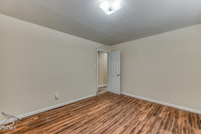 spare room featuring a textured ceiling, baseboards, and dark wood-style flooring