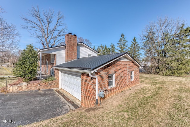 view of side of property featuring metal roof, aphalt driveway, an attached garage, brick siding, and a lawn